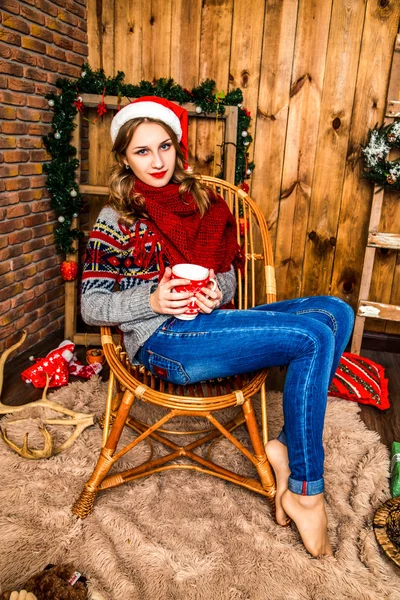 Beautiful blonde girl in a santa hat sitting on a chair — Zdjęcie stockowe