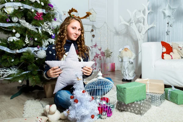 एक सफेद कमरे में क्रिसमस पेड़ के पास बैठी सुंदर लड़की — स्टॉक फ़ोटो, इमेज