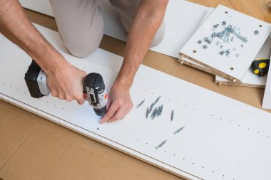 Erkek eller donanımları montaj parçaları ve talimatları ahşap zemine serili beyaz mobilya paneline yapıştırmak için bir tornavida kullanır. Yüksek kalite fotoğraf