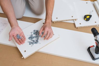 Erkek eller donanımları montaj parçaları ve talimatları ahşap zemine serili beyaz mobilya paneline yapıştırmak için bir tornavida kullanır. Yüksek kalite fotoğraf