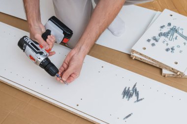 Erkek eller donanımları montaj parçaları ve talimatları ahşap zemine serili beyaz mobilya paneline yapıştırmak için bir tornavida kullanır. Yüksek kalite fotoğraf