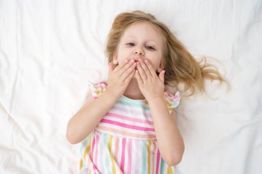 Yatağa uzanmış bir kız, elleri yüzüne yakın bir şekilde öpüşür ve neşeli, neşeli bir çocukluk anı aile hayatı reklamında geniş bir ağız açar. Yüksek kalite fotoğraf