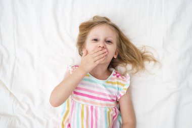 Yatağa uzanmış bir kız, elleri yüzüne yakın bir şekilde öpüşür ve neşeli, neşeli bir çocukluk anı aile hayatı reklamında geniş bir ağız açar. Yüksek kalite fotoğraf