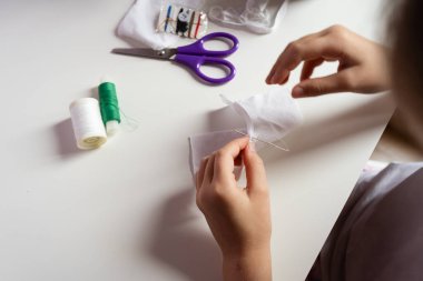 Çocuk elleri, mor makas ve makaralarla beyaz kumaş ve iplik dikiyor. Hobi olarak el yapımı proje konsepti üretiyorlar. Yüksek kalite fotoğraf