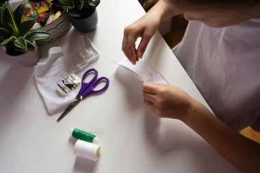 Çocuk elleri, mor makas ve makaralarla beyaz kumaş ve iplik dikiyor. Hobi olarak el yapımı proje konsepti üretiyorlar. Yüksek kalite fotoğraf