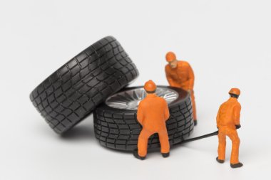 Atölye lastiği provası konsepti. Minyatür tamirciler oyuncak araba tekerleğini tamir ediyor. Kapatın..