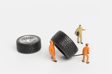 Atölye lastiği provası konsepti. Minyatür tamirciler oyuncak araba tekerleğini tamir ediyor. Kapatın..