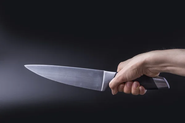 The concept of hand holding a large knife blade upwards diagonally on black background.