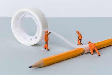 The concept of a collective solution to any problem. Miniature toy repair a broken pencil. Workers perform disposal of the Chief. Close-up view. clipart