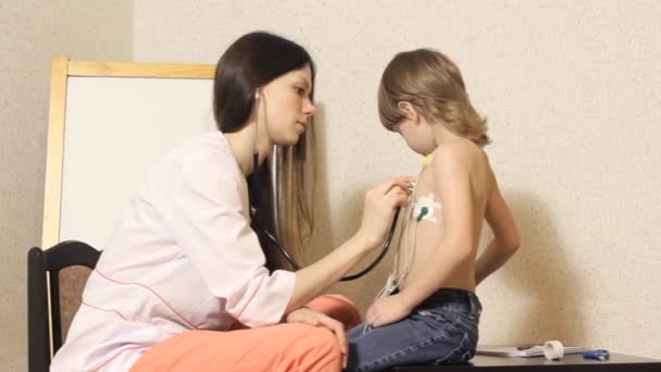 Kvinnan kardiolog bedriver mottagning och undersöka pojken — Stockvideo