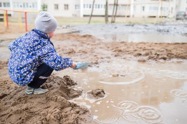 Çamurlu su birikintisi içinde oynayan çocuk