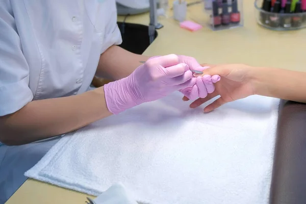 Manicurist master cleaning cuticle using manicure pusher tool, hands closeup. — Stock Photo, Image