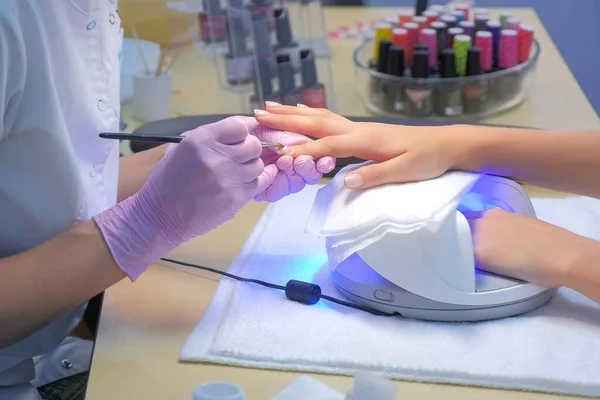 Manicure meester schilderen klanten nagels gel schellak, een andere hand in UV-lamp. — Stockfoto