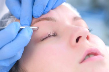 Güzellik uzmanı, kadın için cımbızla kaşlarını yoluyor..