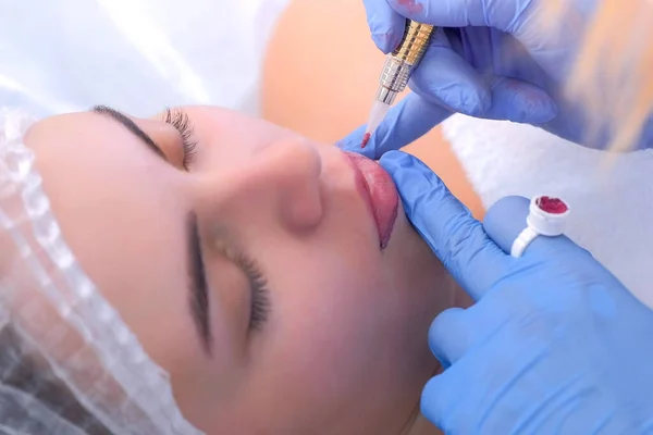 Cosmetologist making lips microblading procedure for girl using tattoo machine.