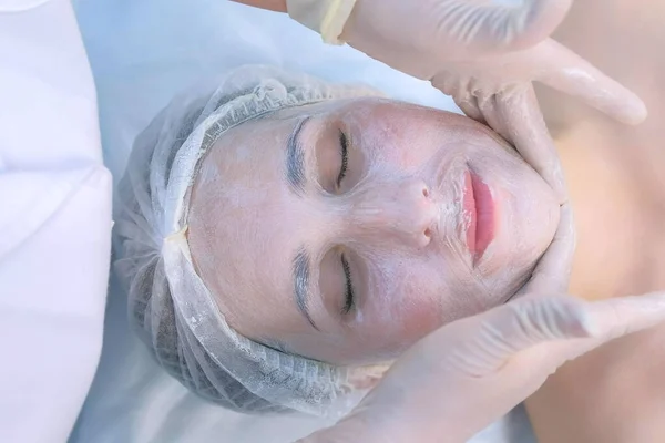 Estetista facendo massaggio facciale con maschera idratante sul viso della donna, primo piano. — Foto Stock