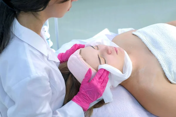 Cosmetoloog veegt hydraterende masker van vrouwen gezicht met behulp van warme handdoek. — Stockfoto