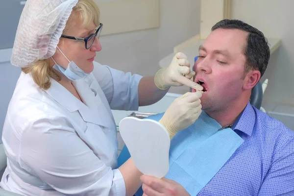 Mujer dentista está enseñando al hombre a limpiar los dientes con hilo dental en la odontología. — Foto de Stock