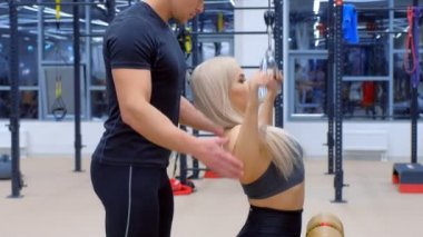 Antrenörlü sporcu bir kadın eğitim makinesinde kol kasları için egzersiz yapıyor..