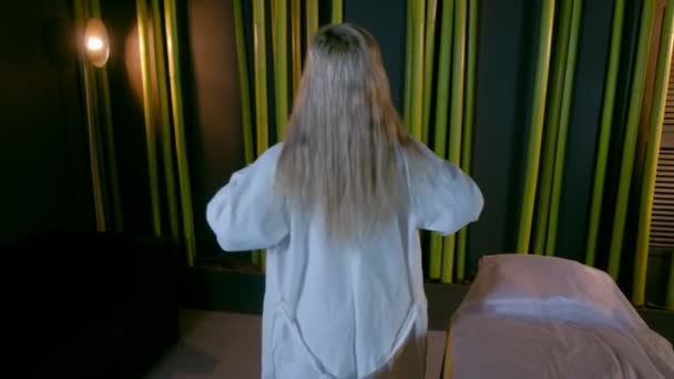 Femme blonde dans le salon de spa enlève la robe se préparant aux procédures, vue de dos. — Video