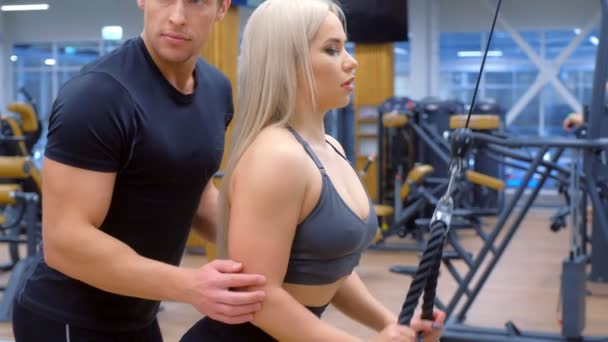 Femme sportive avec entraîneur fait de l'exercice pour les muscles biceps sur la machine d'entraînement. — Video