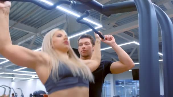 Kvinna gör pull-ups med brett grepp i gymmet med personlig tränare på träning. — Stockvideo