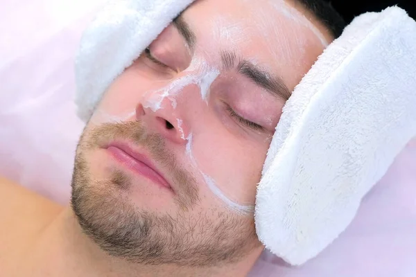 Косметолог стирает увлажняющую маску с лица человека с помощью махровых варежок. — стоковое фото