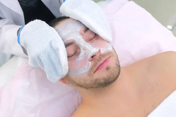 Cosmetologist wipes moisturizing mask from mans face using terry mittens.