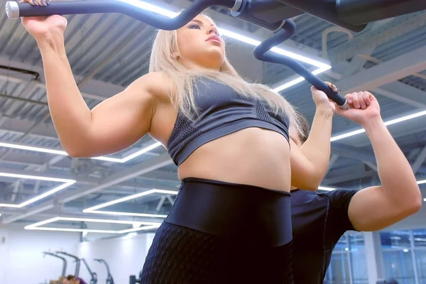 Mujer está haciendo pull-ups con amplio agarre en el gimnasio con entrenador personal en el entrenamiento. —  Fotos de Stock