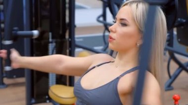 Spor salonundaki kadın antrenörle antrenör arasında kelebek egzersizi yapıyor..