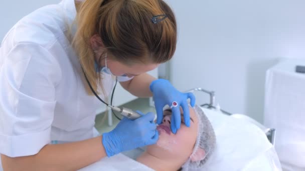 Esteticista aplicando maquillaje permanente en labios de mujer dibujo usando máquina de tatuaje. — Vídeos de Stock