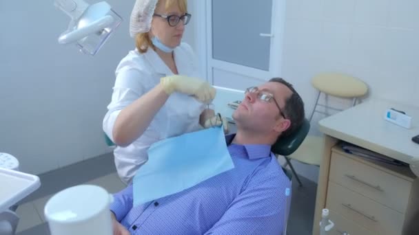 歯科医の女性は、歯科椅子に座っている男の予防検査を行います. — ストック動画