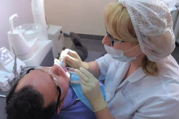 El dentista está aplicando gel azul en los dientes de los hombres para encontrar sarro dental y caries. — Foto de Stock
