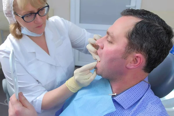 Mujer dentista está enseñando al hombre a limpiar los dientes con hilo dental en la odontología. — Foto de Stock