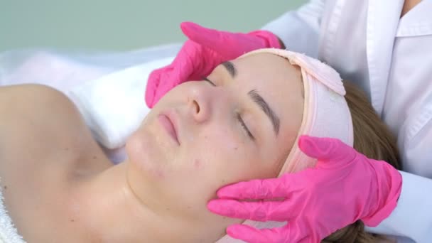 클리닉에서 외과의사가 젊은 여성에게 얼굴 마사지를 해 주는 모습, 클로즈업으로 본 모습. — 비디오