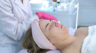 Güzellik uzmanı sıcak havlu kullanarak kadınların yüzündeki nemlendirici maskeyi siliyor..