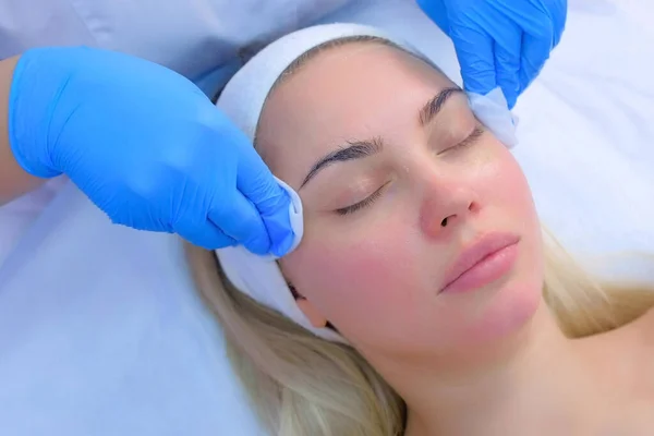 Cosmetoloog arts veegt vrouwen gezicht met behulp van antibacteriële servetten, close-up. — Stockfoto