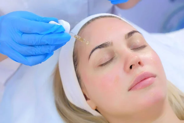 Cosmetoloog is het aanbrengen van hydraterende olie op vrouwen gezicht, close-up portret. — Stockfoto