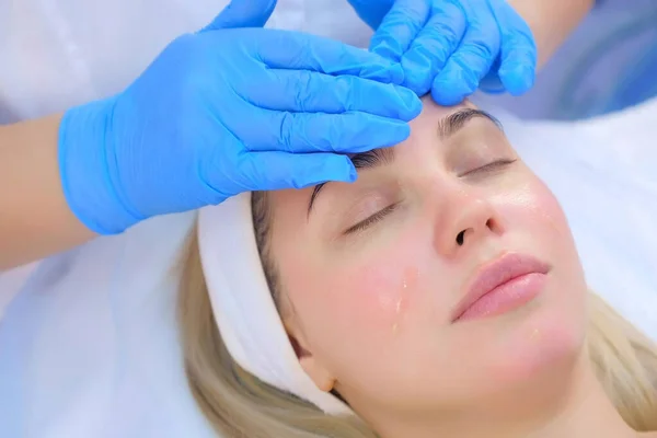 Beautician is applying moisturizing oil on womans face, closeup portrait.