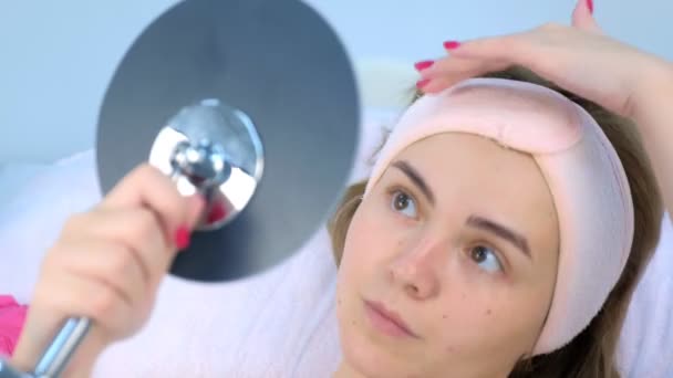 Retrato de una paciente joven mirando el espejo después de la limpieza de la piel de la cara. — Vídeos de Stock