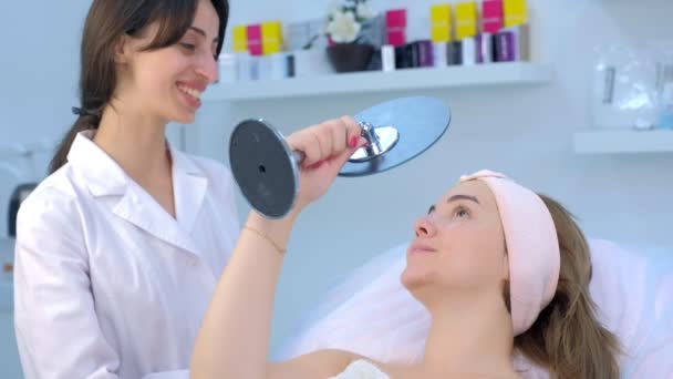 Młoda kobieta pacjent patrząc w lustro po zabiegu oczyszczania skóry twarzy. — Wideo stockowe
