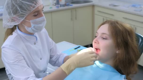 Orthodontiste dentiste mettant rétracteur dans la bouche de la fille, montrant les dents dans le miroir. — Video