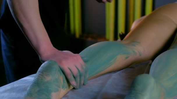 Cosmetólogo hombre aplicando arcilla azul en el cuerpo de las mujeres en las piernas, las manos de cerca. — Vídeo de stock