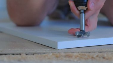 İnsan yonga tahtasına işaretler çizer ve elektrikli matkap kullanarak delik açar.