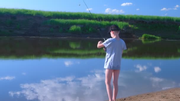 Kind jongen is vissen in de rivier met behulp van spinning rod in de zomer zonnige dag op de natuur. — Stockvideo