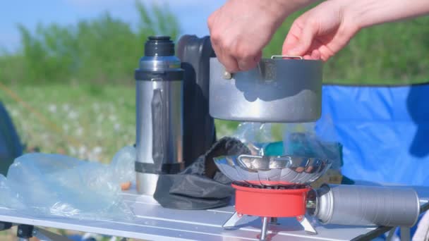 Az ember főzés élelmiszer segítségével kis gázégő kemping a természetben, kéz közelkép. — Stock videók