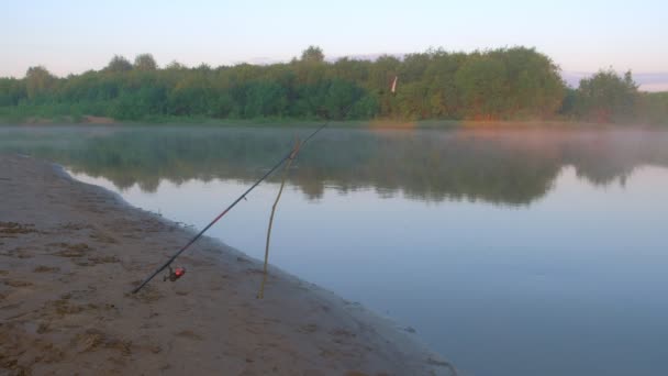 Vara giratória de pesca na margem do rio ao pôr-do-sol no início da manhã. — Vídeo de Stock