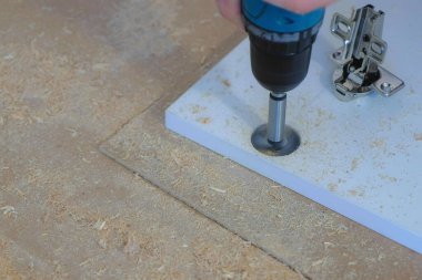 Menteşe yapmak için gardırop kapısında delik açan bir adam mobilya yapıyor..