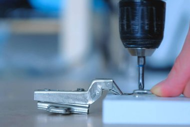 Marangoz elektrikli tornavida kullanarak mobilya kapısına menteşe yapıyor..