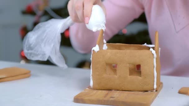 Mulher fazendo gingerbread casa cola detalhes açúcar doce gelo, mãos closeup. — Vídeo de Stock